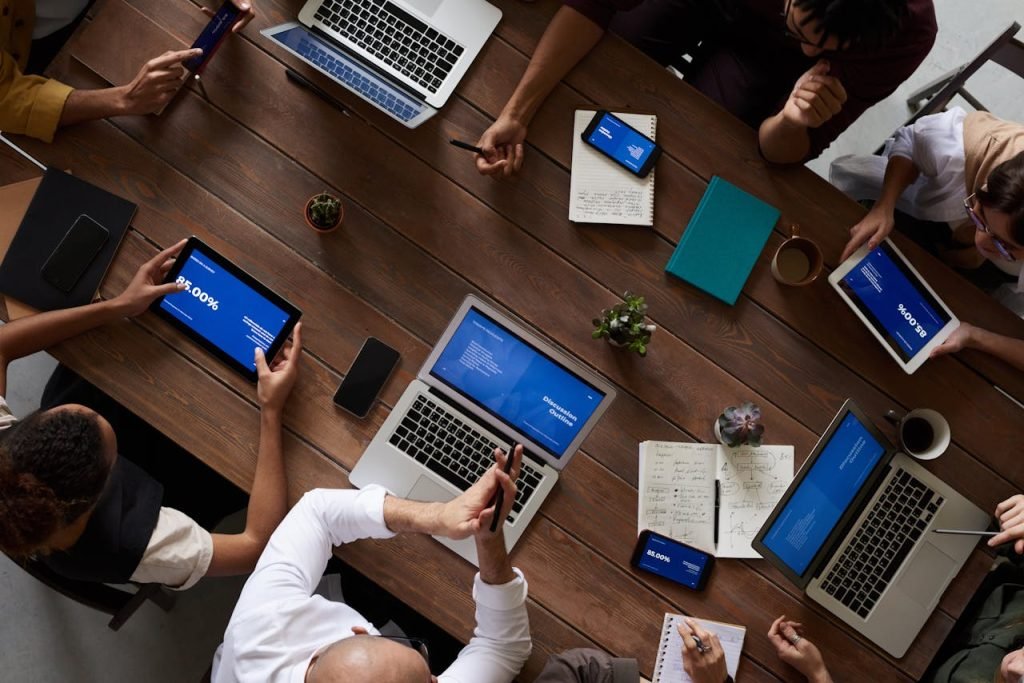 people-having-business-meeting-together-3183183 Overhead view of a diverse team discussing around a wooden table, using technology.