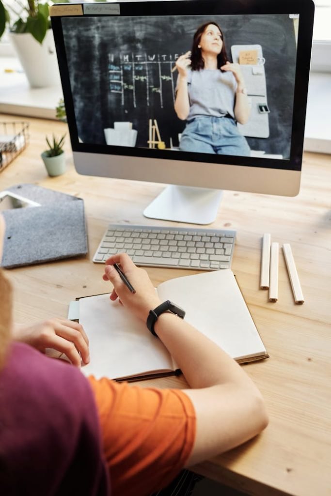 person-using-silver-imac-while-holding-pencil-4144228 Student attending virtual class on a computer, taking notes at home.